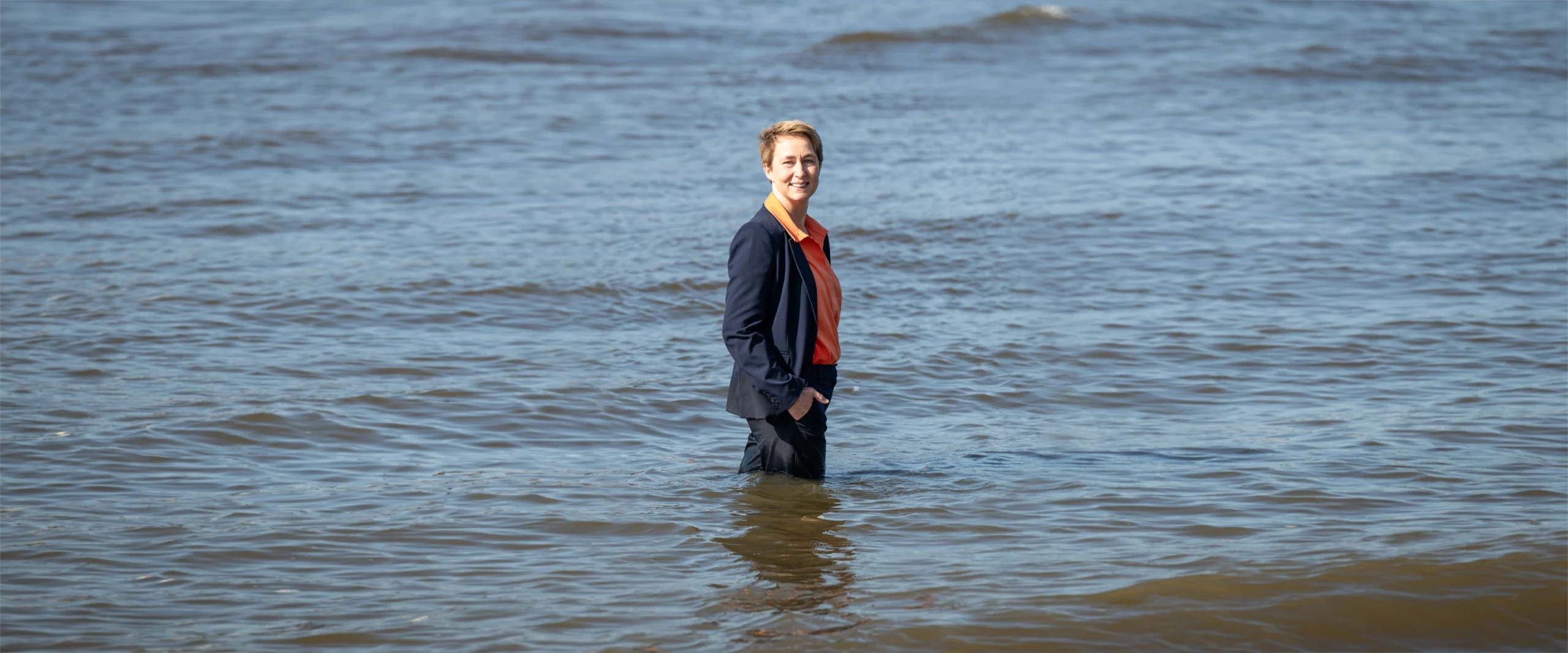 Peggy Steinhauser im Wasser stehen mit einem blauen Anzug einem orangen Hemd.